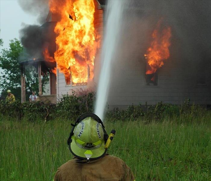 Firefighter spraying a burning house with water